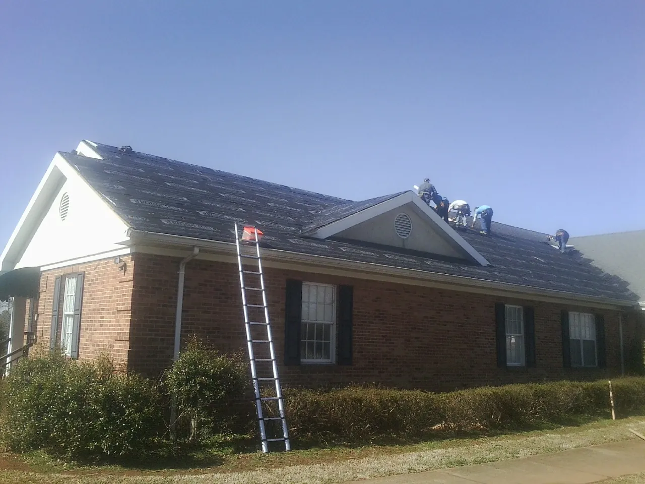 Crew tearing shingles off a brick ranch roof with a ladder set — Emergency Roof Repair work by our crew in Nahant