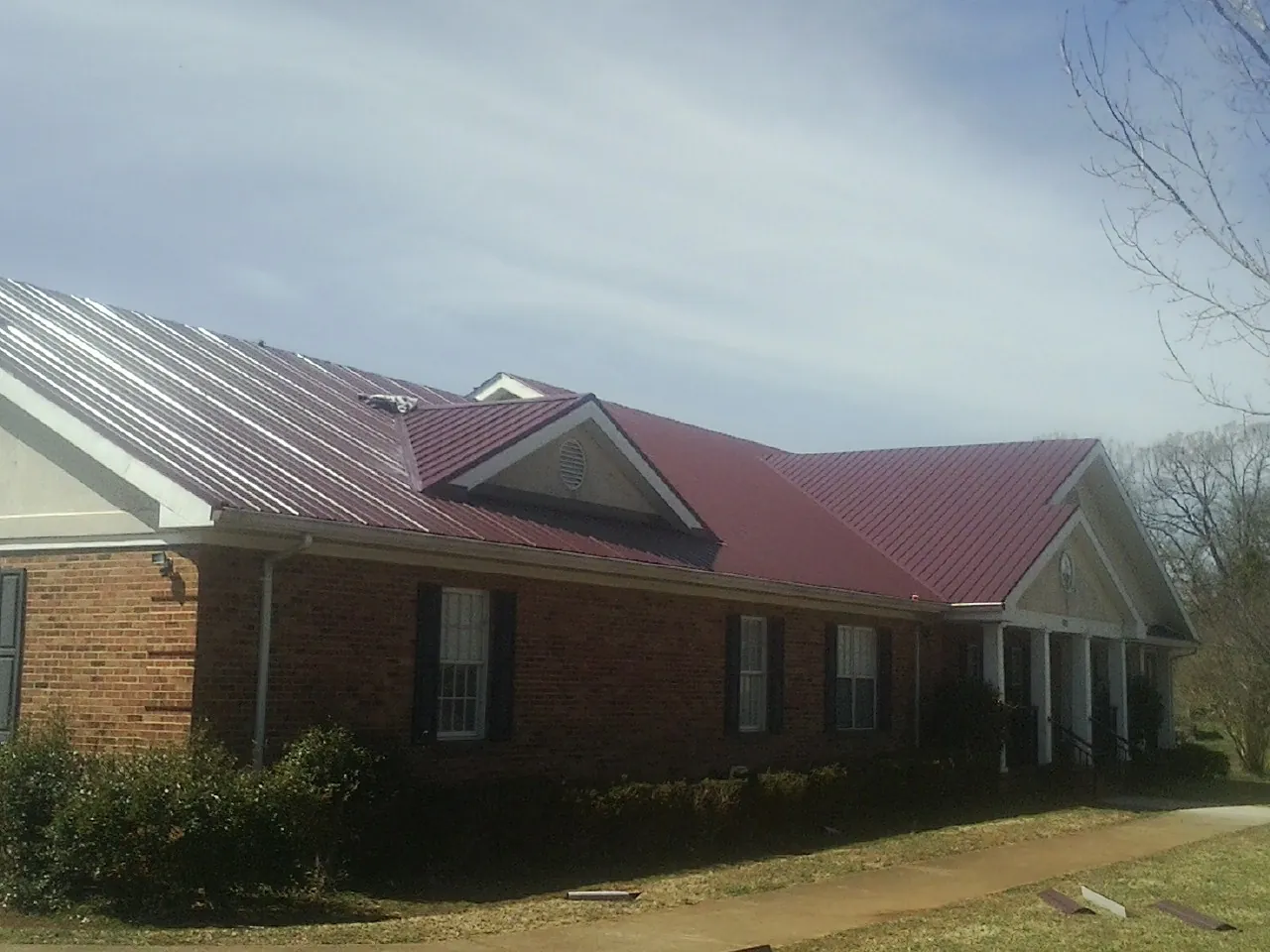Red metal roof with gabled entries on a long brick building, from a Hail Damage Roof Repair job in Nahant