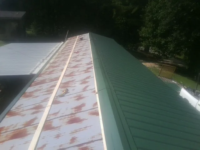 Old rusted panels beside newly installed green metal roofing — Wind Damage Roof Repair by Roofing Brothers in Nahant