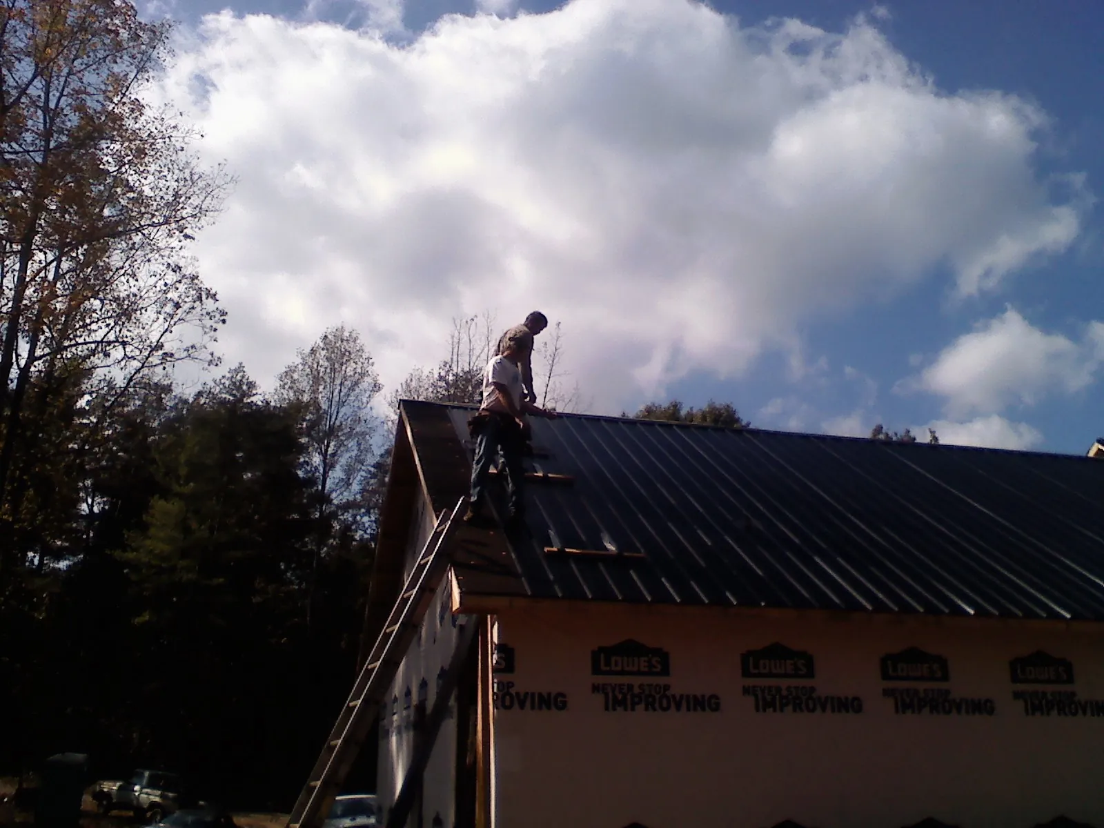 Roofer fastening dark metal panels high against a cloudy sky, from a Roof Inspection job in Nahant