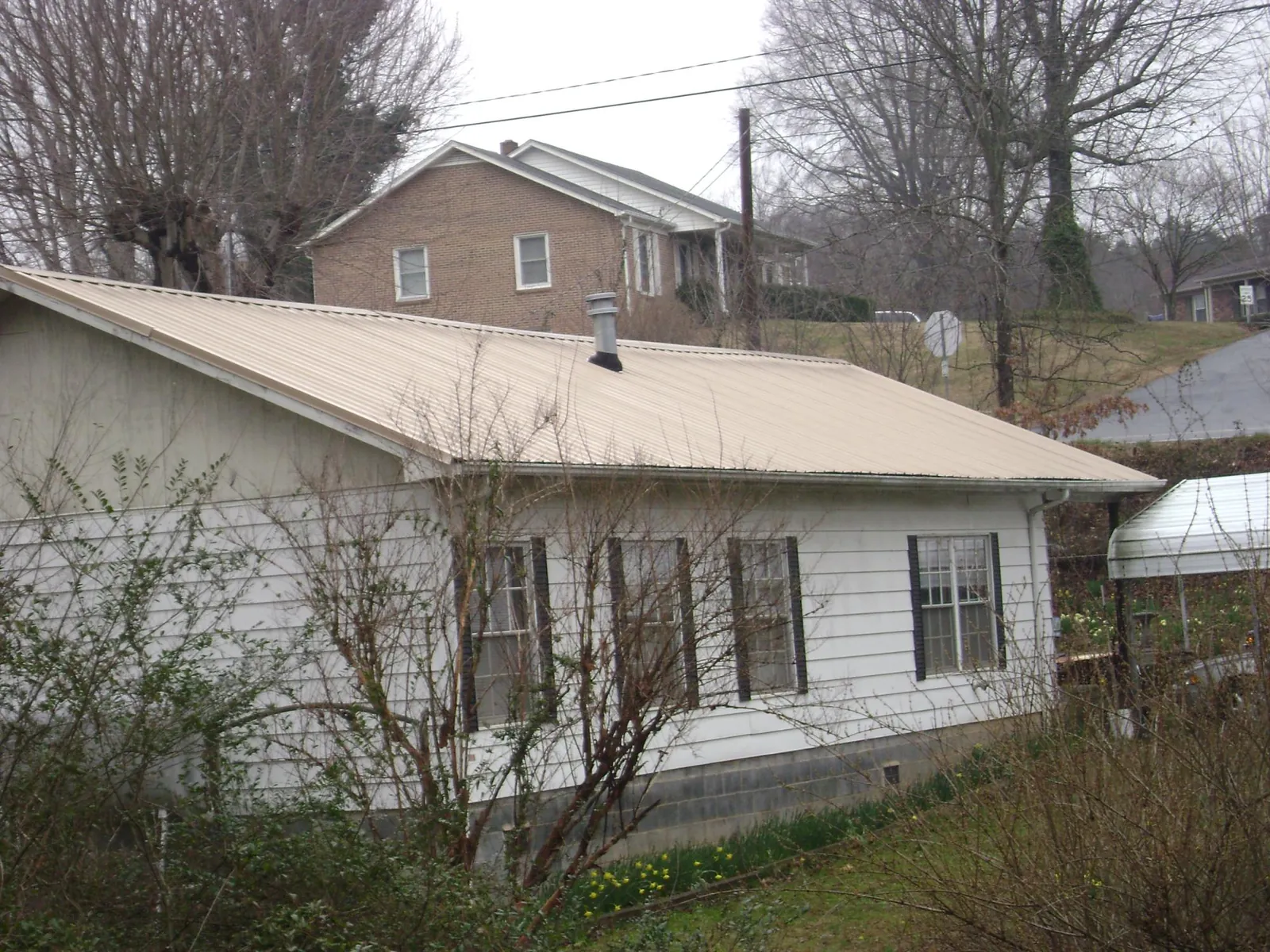 Tan metal roof on a white sided house set into a hillside — Commercial Roofing by Roofing Brothers in Nahant